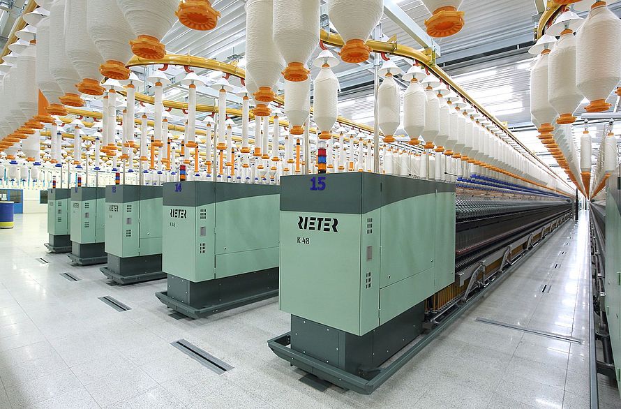 A modern industrial textile line with rows of large spinning machines producing thread at scale.
